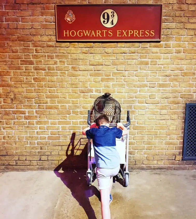 Boy pushing a trolly into a wall with the sign 9 3/4 Hogwarts Express