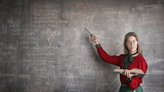 a female teacher standing in front of a black chalk board teaching students