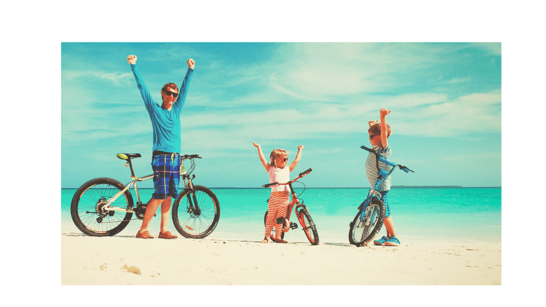 A dad and 2 kids having a bike ride on the beach.