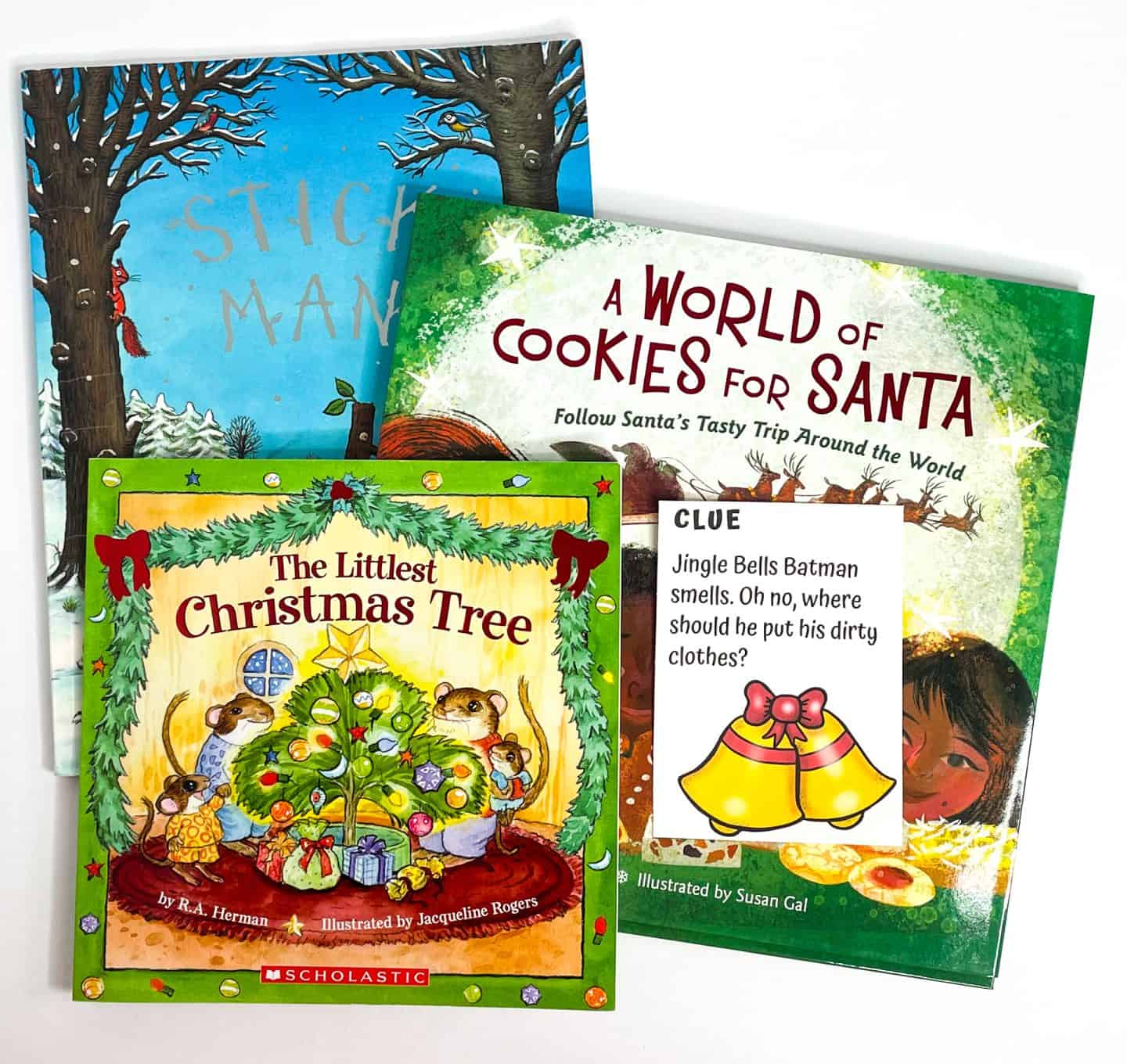 Three festive children's books—Stick Man, A World of Cookies for Santa, and The Littlest Christmas Tree—are stacked together with one of the printable Christmas scavenger hunt clues placed on top. The clue reads, “Jingle Bells Batman smells. Oh no, where should he put his dirty clothes?” with an illustration of yellow bells tied with a red bow. Perfect visual for a holiday activity featuring Christmas scavenger hunt clues alongside classic storybooks.

