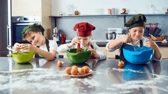 3 kids with chefs hats mixing a cake. 