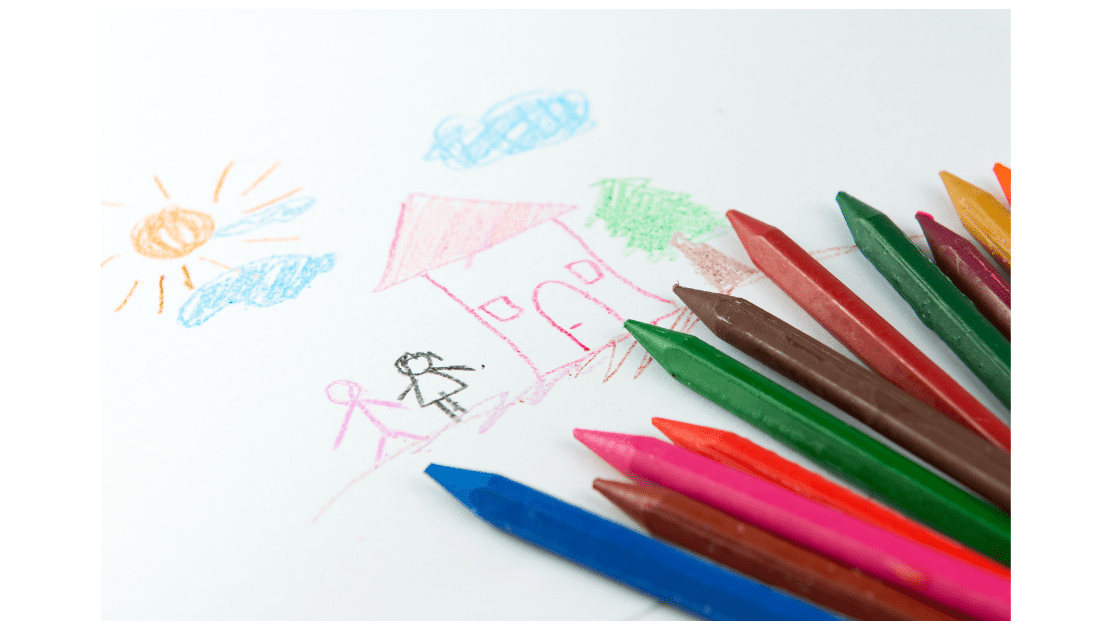 A child's crayon drawing of a sun, clouds, and a house with a family, alongside colored pencils, depicting a simple and happy home scene, illustrating creativity in early childhood education.