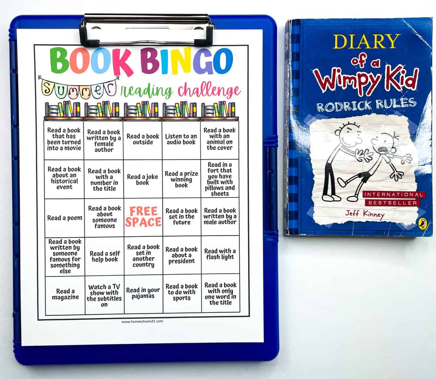 A summer reading challenge "Book Bingo" sheet is clipped to a blue clipboard, featuring colorful categories like "Read a book with a number in the title" and "Read in your pajamas." Next to it is the book Diary of a Wimpy Kid: Rodrick Rules by Jeff Kinney, with its blue illustrated cover showing two cartoon characters and labeled as an international bestseller.