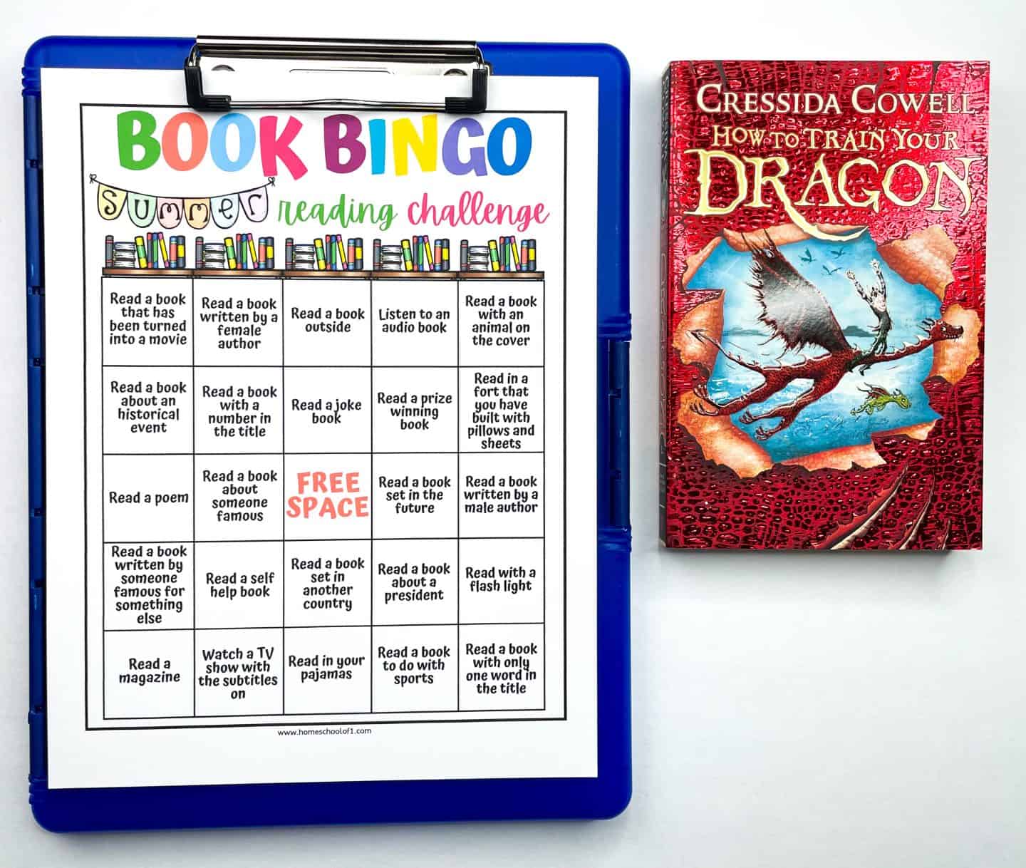A summer reading challenge book bingo sheet on a clipboard sits next to a copy of How to Train Your Dragon by Cressida Cowell. The bingo sheet features colorful text and prompts like "Read a book outside" and "Read a book with an animal on the cover." The red book cover displays a dragon flying across a map design.