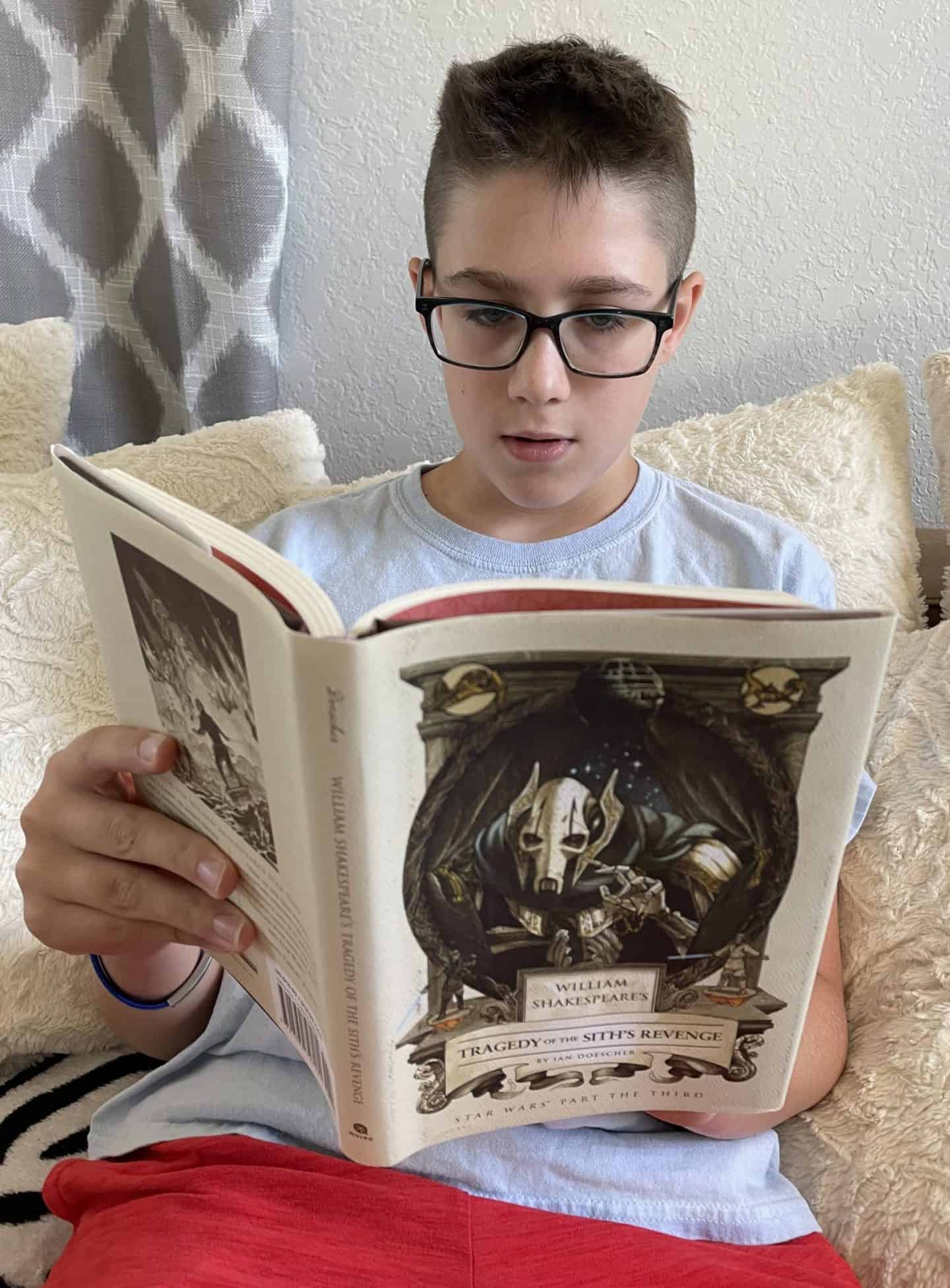teenage boy wearing glasses reading William Shakespeare's Tragedy of the Sith's Revenge by Ian Doescher