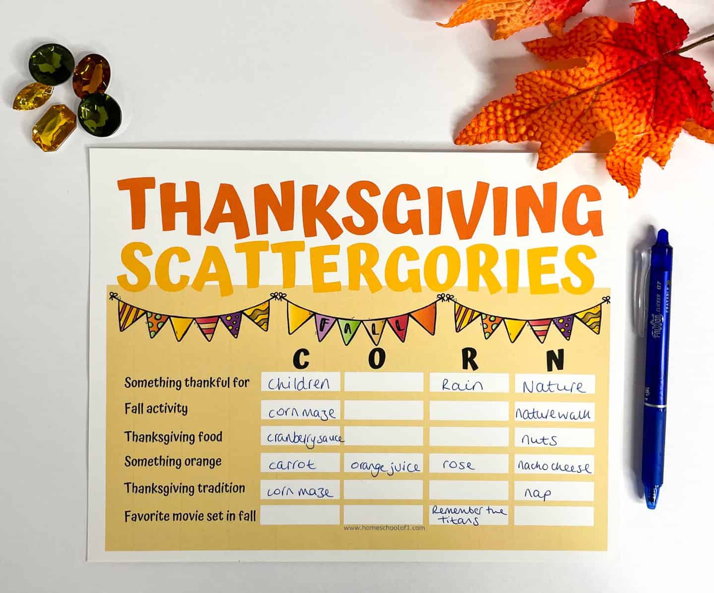 A filled-in Thanksgiving Scattergories card using the word “CORN,” featuring handwritten answers like "children," "corn maze," and "cranberry sauce." Surrounded by colorful fall leaves, gem decorations, and a blue pen, this festive activity adds fun to any Thanksgiving gathering.








