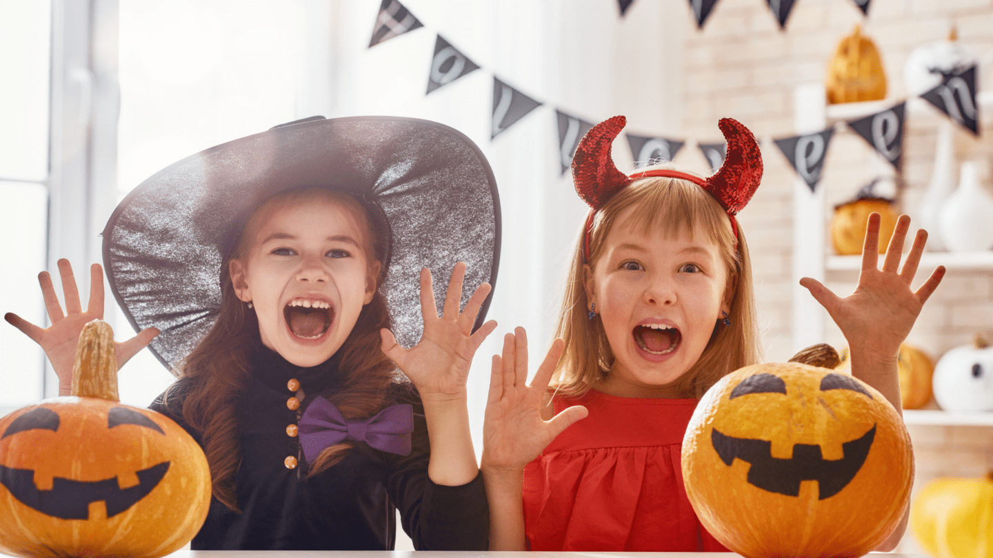 2 girls wearing halloween costumes in front of 2 jack o lanterns