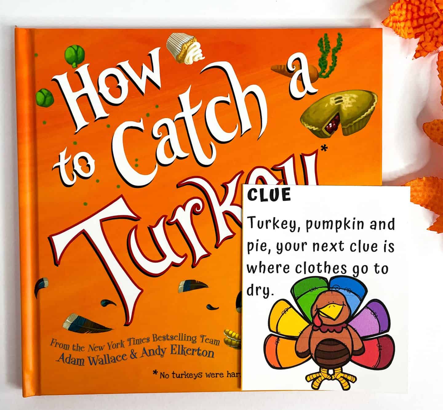 A children's Thanksgiving book titled How to Catch a Turkey by Adam Wallace and Andy Elkerton is shown with a bright orange cover and festive illustrations of food. In front of the book is a colorful scavenger hunt clue card featuring a rainbow-feathered turkey and a rhyme that reads: “Turkey, pumpkin and pie, your next clue is where clothes go to dry.”