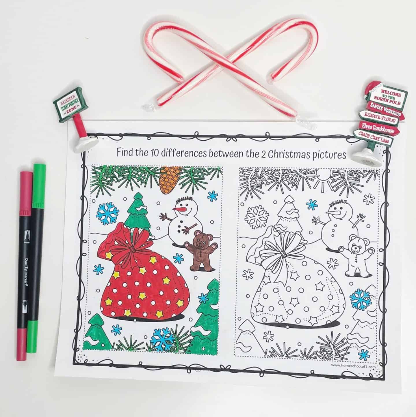 A festive spot-the-difference coloring page featuring two Christmas-themed illustrations side by side. Each picture shows a red gift sack surrounded by snowflakes, trees, a snowman, and a teddy bear, with the left image partially colored in. Decorative touches include two candy canes shaped into a heart, red and green markers, and small North Pole-themed signs around the page.