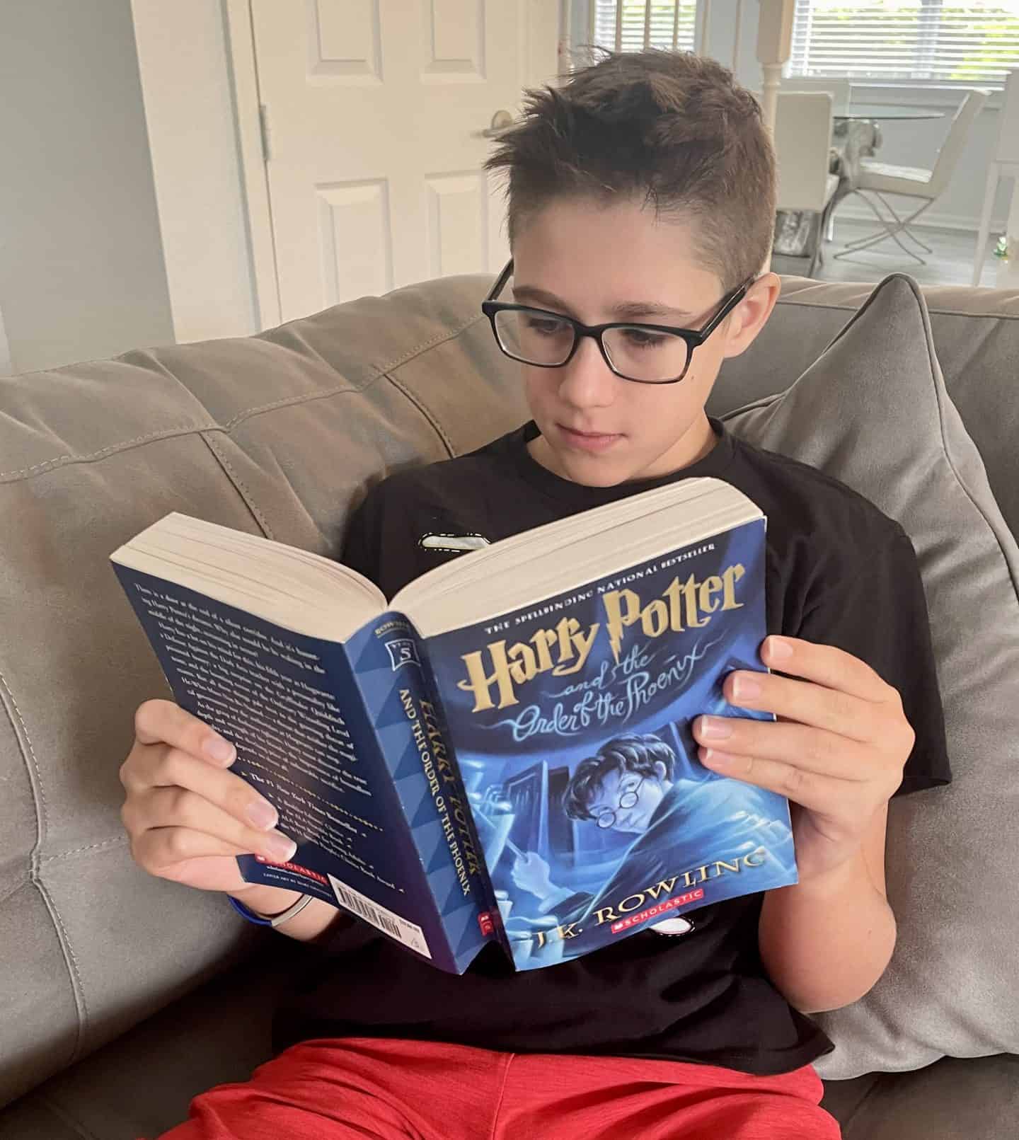 13 year old boy wearing glasses sitting in his living room reading Harry Potter and the Order of the Phoenix