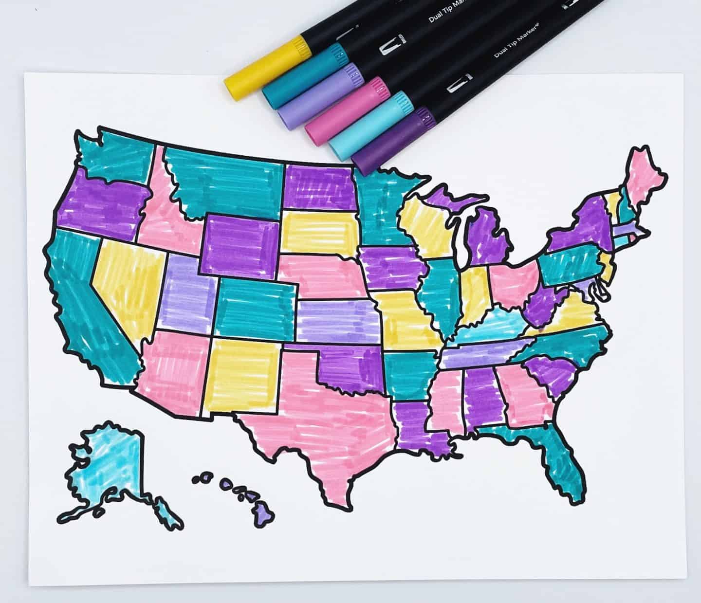 U.S. map coloring page with each state filled in using bright colors like pink, teal, purple, yellow, and light blue, with clear black borders outlining the states. Five uncapped dual-tip markers in matching colors are placed across the top edge of the page.