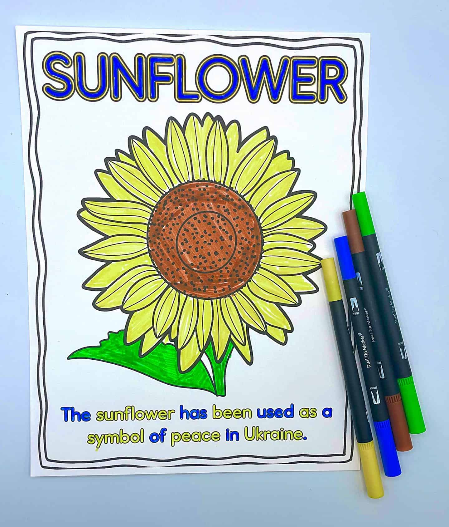 A colored in sunflower coloring sheet in yellow and blue, with the words the sunflower has been used as a symbol of peace in Ukraine also colored in yellow and blue with those color pens to the side.