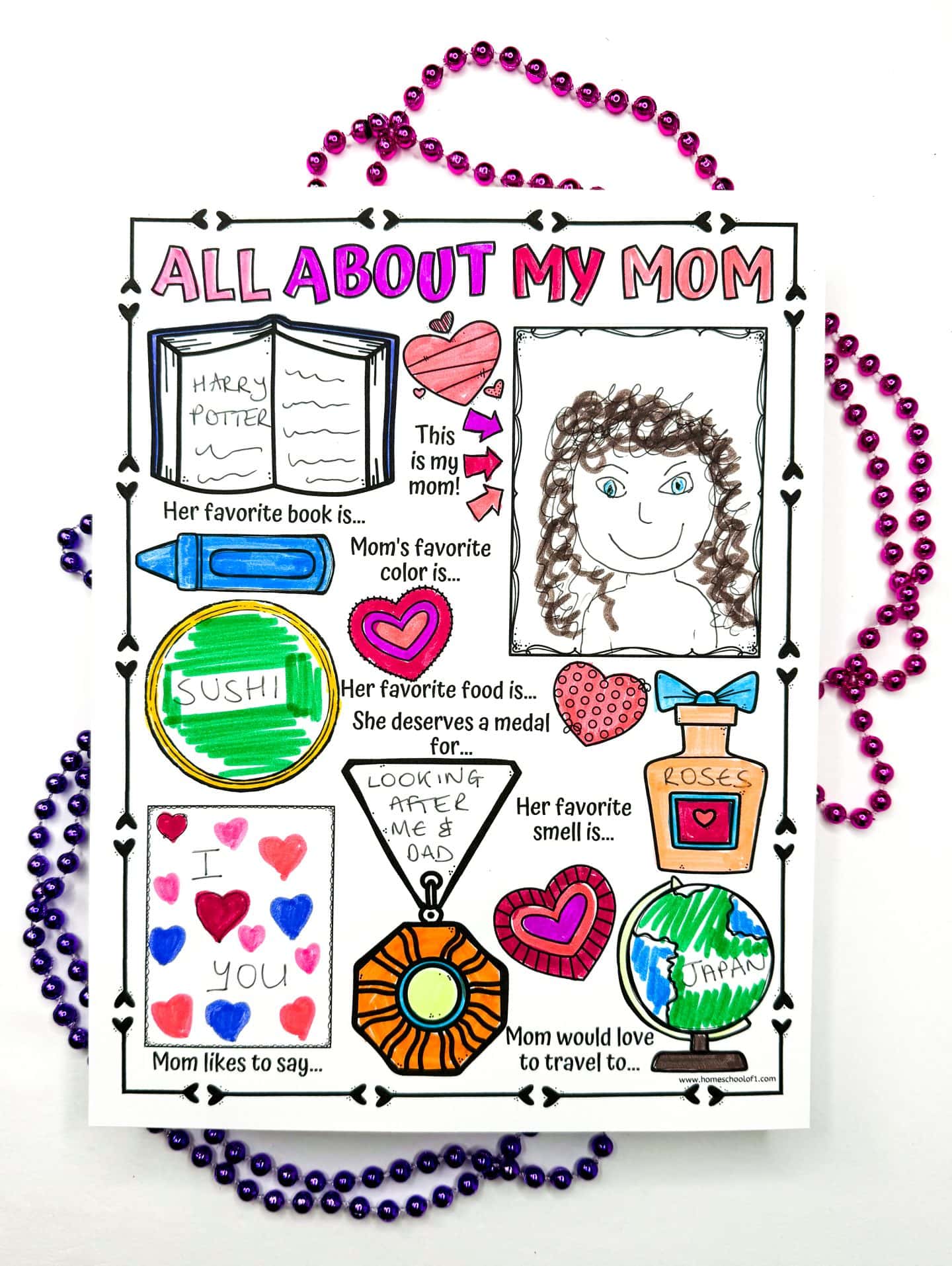 A completed and colored “All About My Mom” printable worksheet, featuring answers written in a child’s handwriting. Mom’s favorite book is Harry Potter, her favorite color is pink, and her favorite food is sushi. She deserves a medal for “looking after me & dad,” loves the smell of roses, and would love to travel to Japan. The drawing includes a childlike portrait, hearts, and the phrase “I ? you” under “Mom likes to say.” Pink and purple beaded necklaces frame the sheet.