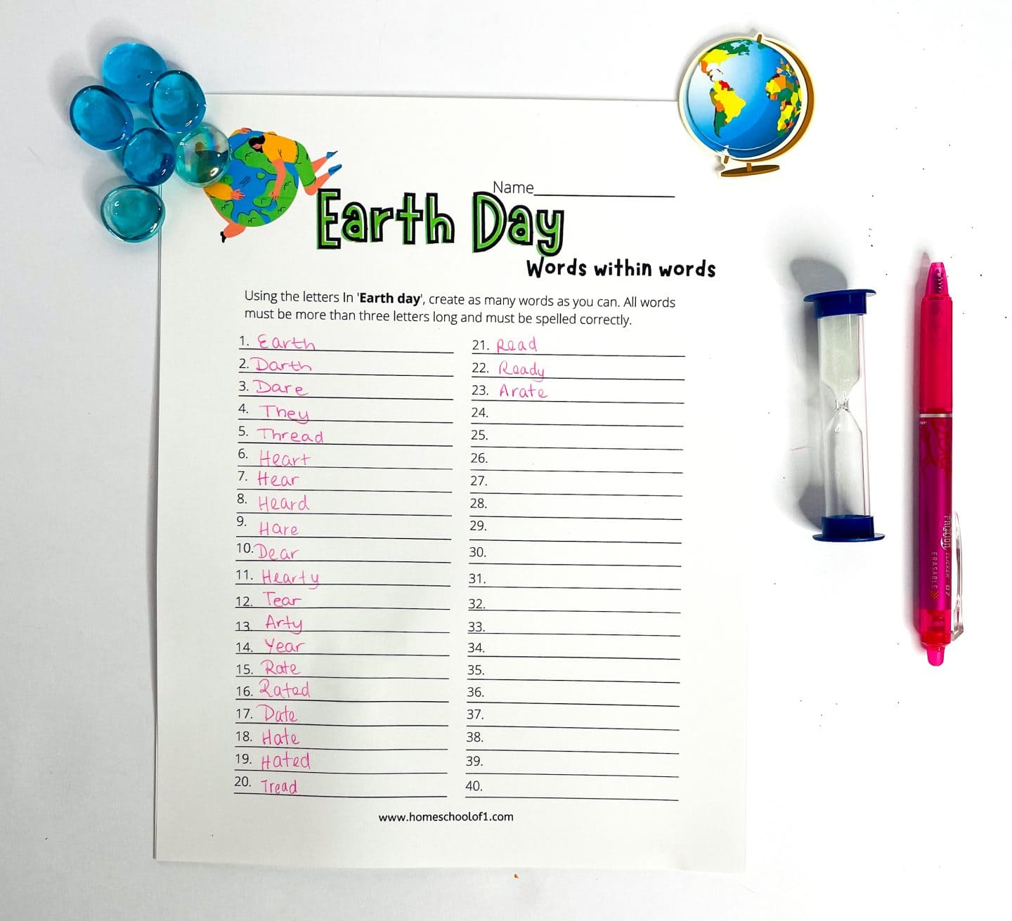 An Earth Day-themed “Words Within Words” worksheet shows 23 handwritten words formed from the letters in “Earth Day.” The sheet features a cartoon image of the Earth with a heart and stars, and is surrounded by blue glass pebbles on the left, a pink pen, and a blue sand timer on the right—adding a playful, educational feel.