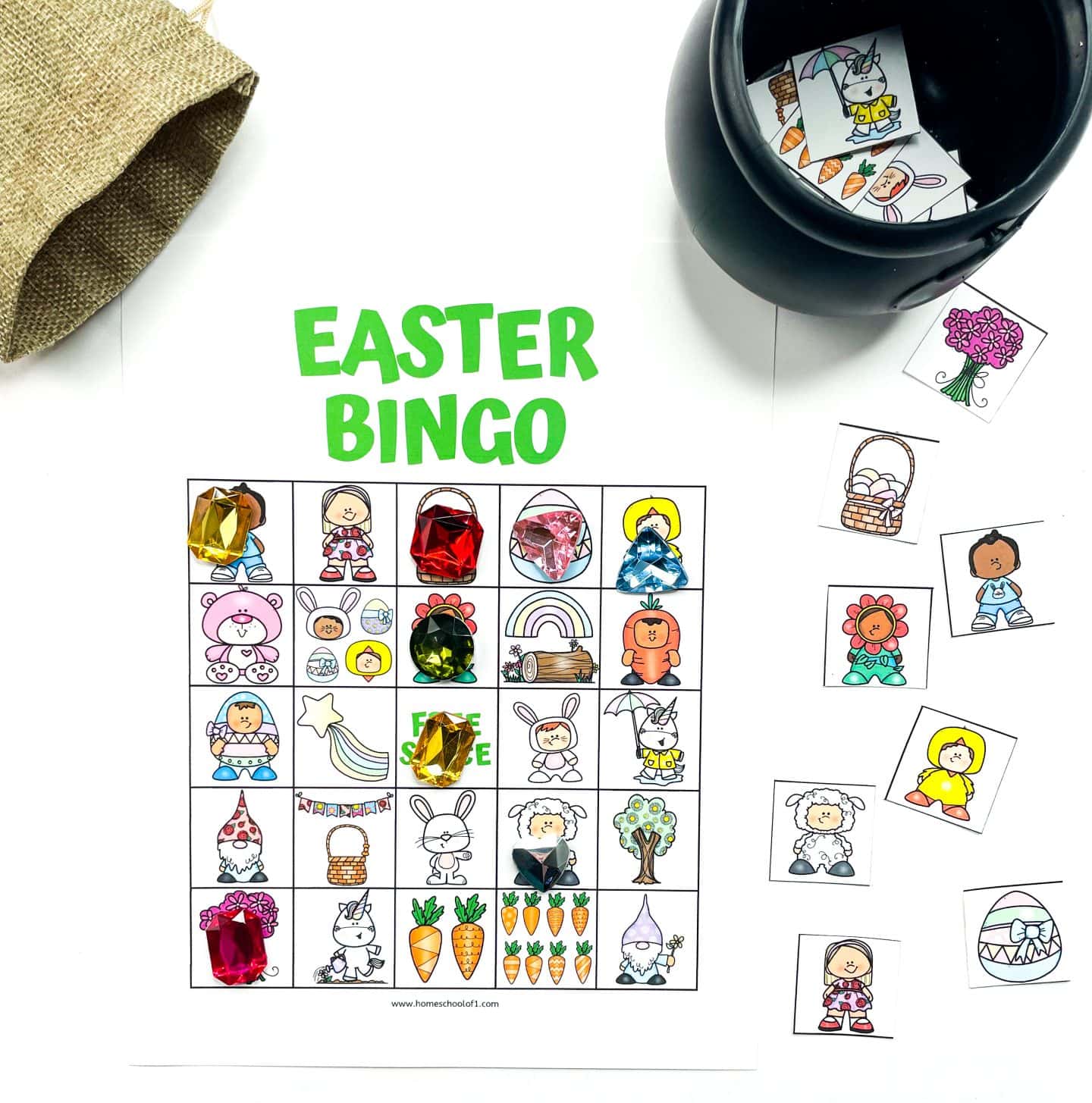 Colorful Easter bingo board in use, with cartoon illustrations of Easter characters and objects such as bunnies, carrots, chicks, baskets, rainbows, and gnomes. Large plastic gem markers cover some squares, and additional bingo calling cards are placed nearby. A small black pot and burlap bag hold the remaining game pieces, making this a fun and festive printable activity