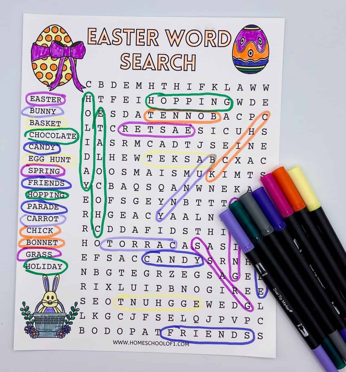 Completed Easter word search printable with fun themed words like “bunny,” “egg hunt,” “chocolate,” and “parade,” each highlighted in colorful marker. The page is decorated with Easter egg illustrations and a bunny in a basket, and six dual-tip markers are laid beside the sheet. 