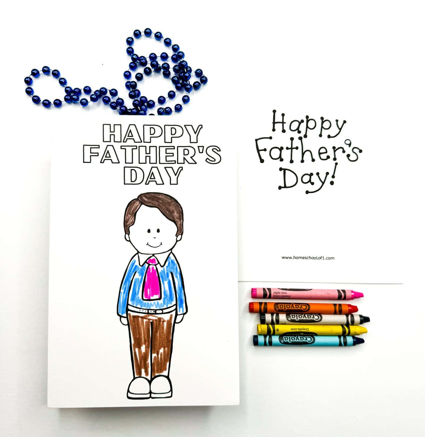 Coloring card for Father's Day featuring a cartoon drawing of a dad wearing a blue shirt, pink tie, and brown pants, with "Happy Father's Day" written above. The card is surrounded by a blue beaded necklace and Crayola crayons, next to another printable card that says "Happy Father's Day!" in playful black font.