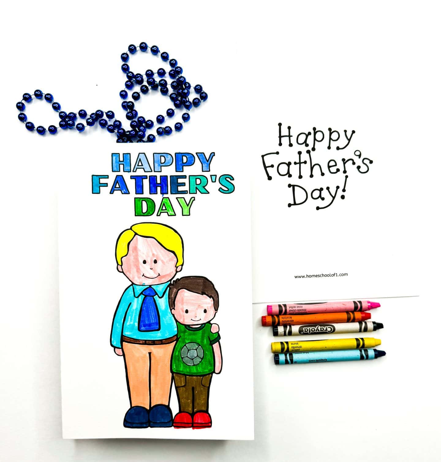 Hand-colored Father's Day card featuring a smiling father and son with the message "Happy Father's Day" in blue and green. The setup includes a blue beaded necklace, additional printable card with "Happy Father's Day!" text, and five Crayola crayons for coloring.