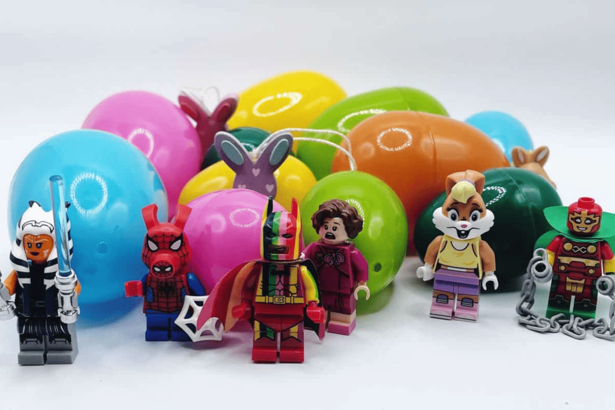 Colorful plastic Easter eggs in the background with an assortment of toy mini-figures lined up in front, including characters resembling superheroes and fantasy figures. This setup showcases fun and healthy non-candy Easter egg filler ideas for kids.