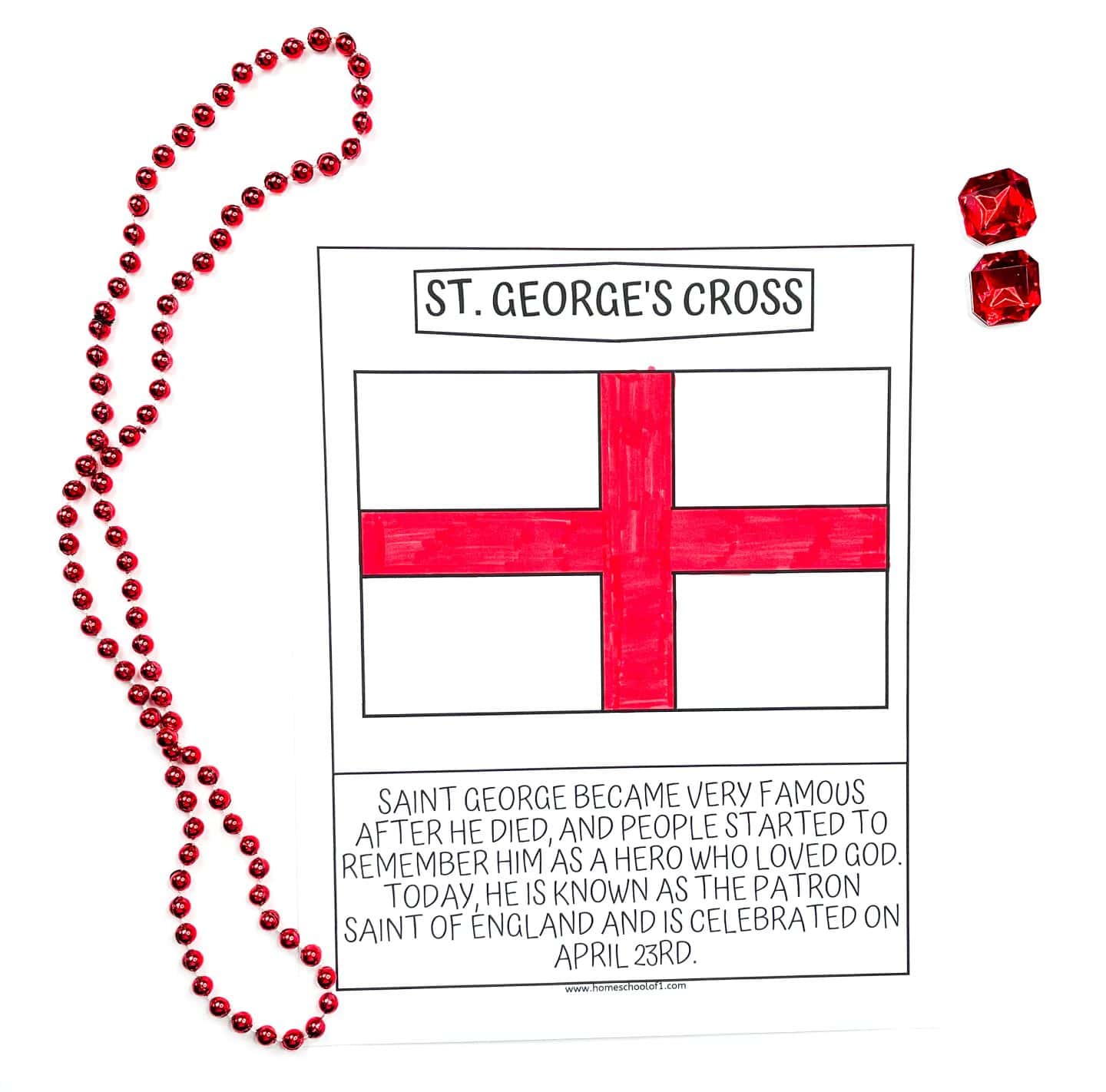 A children’s coloring page titled “St. George’s Cross,” showing a simple illustration of the red cross on a white background that represents the flag of England. The text below explains that Saint George became well-known after his death as a hero devoted to God, and he is now recognized as the patron saint of England, celebrated on April 23rd. The page is surrounded by a red bead necklace and two red faux gemstones.

