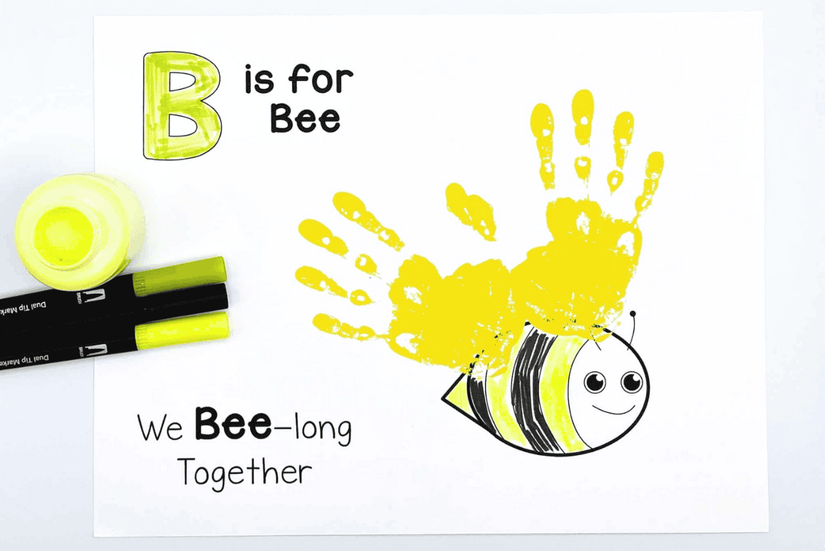 Yellow handprints form wings on a smiling bee with the letter B colored green, a fun preschool “B is for Bee” handprint craft.