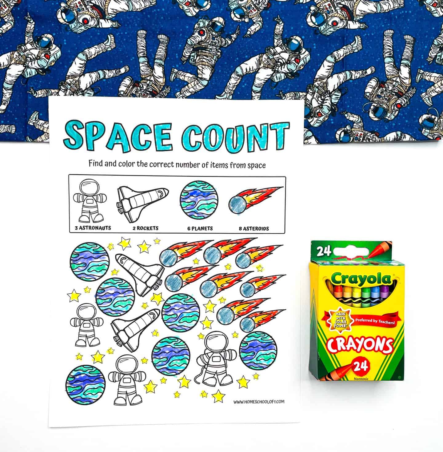 A preschool worksheet titled "Space Count" featuring colorful illustrations of rockets, planets, asteroids, and astronauts. Children are instructed to find and color 3 astronauts, 2 rockets, 6 planets, and 8 asteroids. A box of Crayola crayons and a blue space-themed fabric with astronaut illustrations are placed beside and above the worksheet.