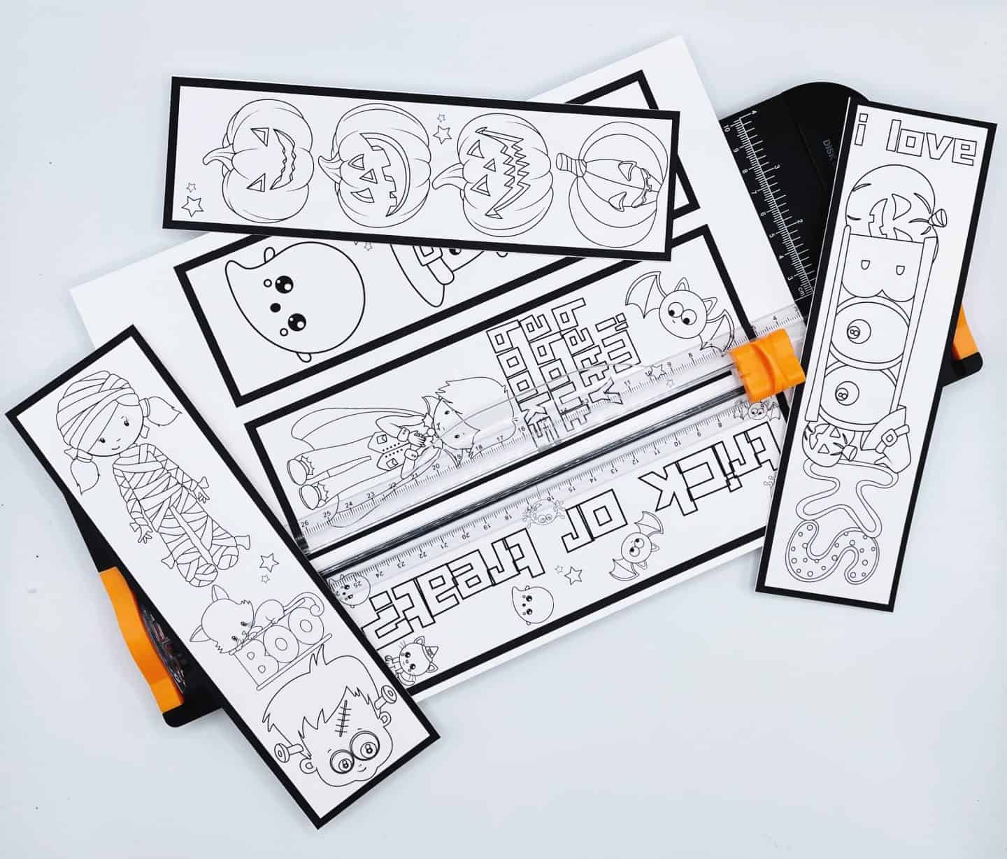 A set of Halloween-themed coloring bookmarks in black and white placed on a paper trimmer. The bookmarks feature cute Halloween illustrations including pumpkins, a ghost, a vampire, a mummy, a test tube with the word "BOO," and the phrase "trick or treat."