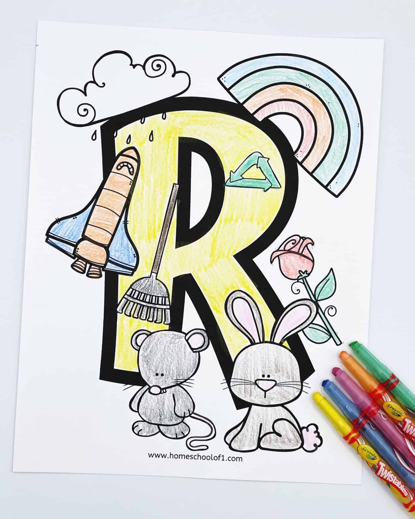 A printable letter "R" coloring page for kids featuring a large yellow "R" outlined in black, surrounded by illustrations of a rocket, rainbow, rose, rake, raindrops, rabbit, and rat. The page is partially colored, with a set of colorful Crayola Twistables markers lying nearby.