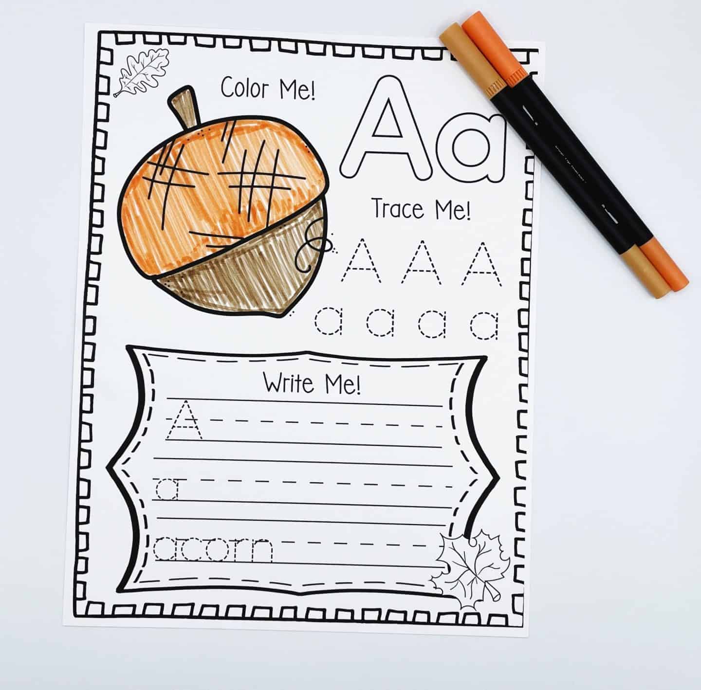 A fall alphabet worksheet for the letter A, featuring a large acorn illustration to color, uppercase and lowercase letter tracing, and space to practice writing the word “acorn.” Two colored markers lie beside the page, emphasizing the autumn theme.








