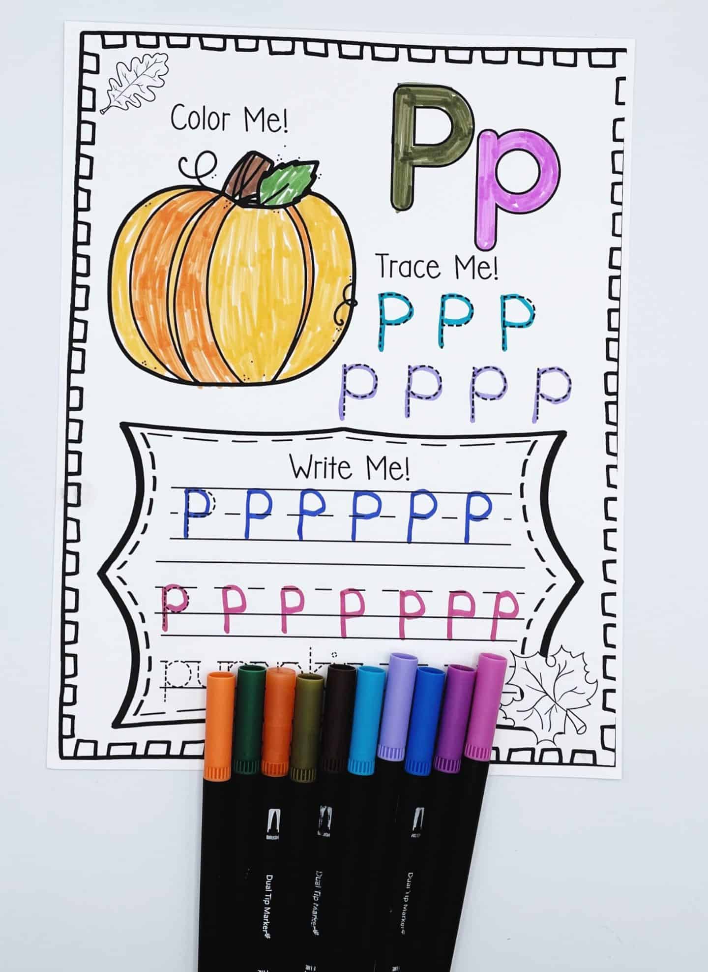 Fall alphabet worksheet for the letter P featuring a pumpkin to color, uppercase and lowercase P tracing, and handwriting lines for writing “pumpkin.” A colorful set of markers is placed along the bottom of the page for a fun, hands-on learning activity.