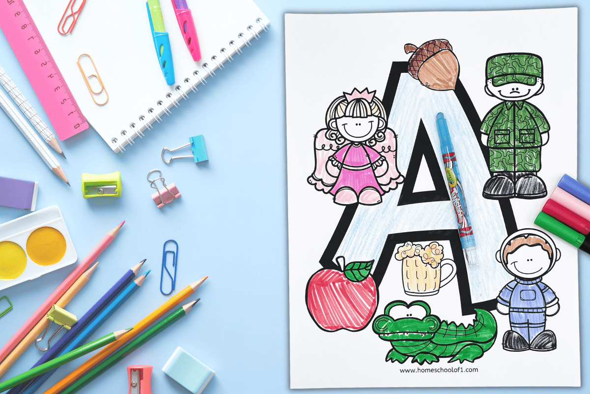 Letter A coloring page featuring a large, bold letter A surrounded by A-themed illustrations, including an apple, alligator, acorn, ale mug, army soldier, and children in costume. The page is partially colored and displayed with crayons, pencils, and art supplies on a light blue background.