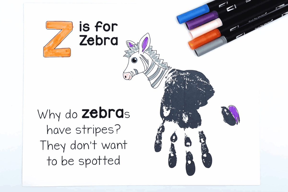 Z is for Zebra educational craft featuring a zebra head illustration and a child’s black handprint forming the zebra’s body. The text reads: 'Why do zebras have stripes? They don't want to be spotted.' Four colored markers—blue, purple, peach, and orange—are placed in the top right corner, suggesting this is a fun and creative learning activity for kids.
