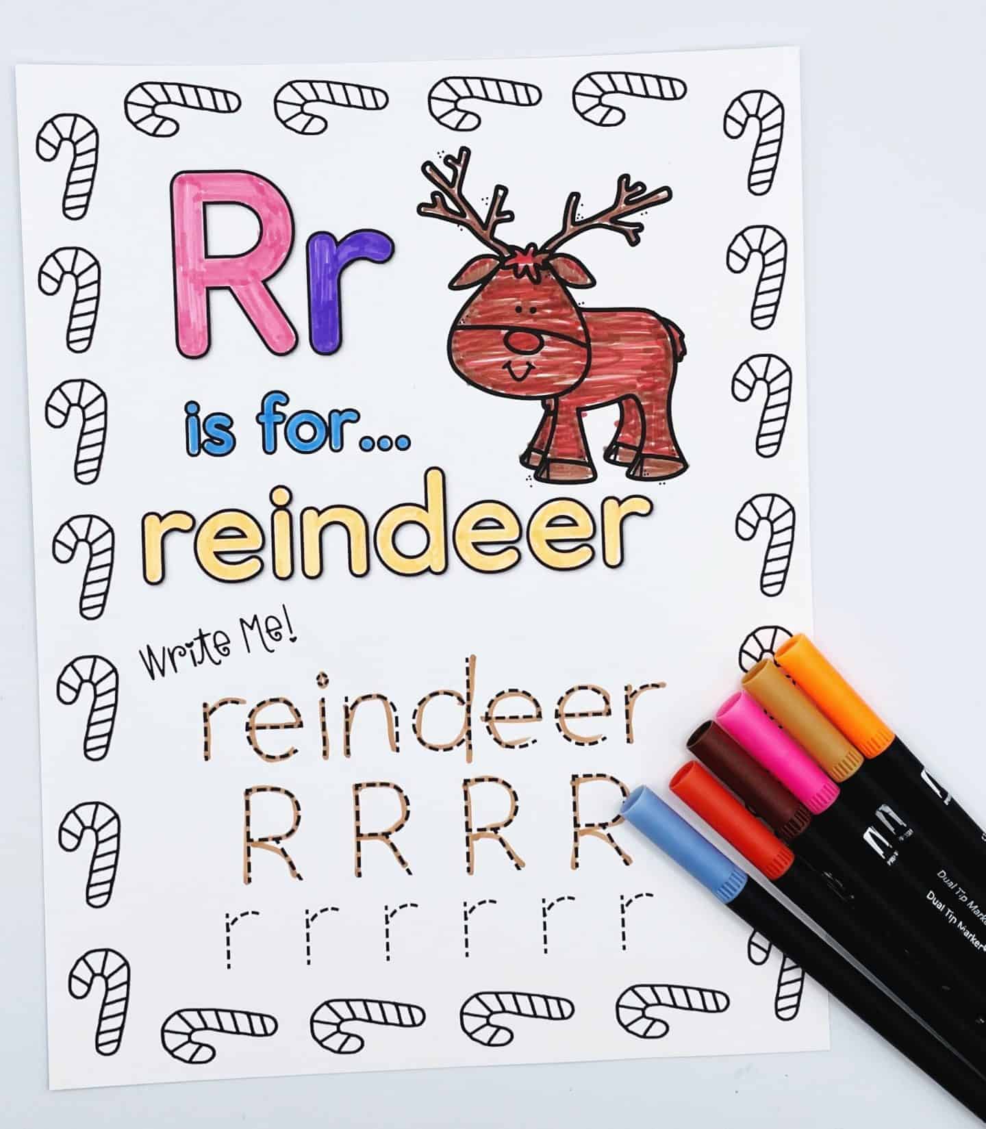 Christmas-themed alphabet worksheet for the letter R, featuring “Rr is for… reindeer.” A cute, smiling reindeer is colored brown next to the word "reindeer" in large yellow letters. The page includes traceable practice for the word "reindeer" and uppercase and lowercase R’s, all surrounded by a candy cane border. Several colorful markers are shown in the corner.