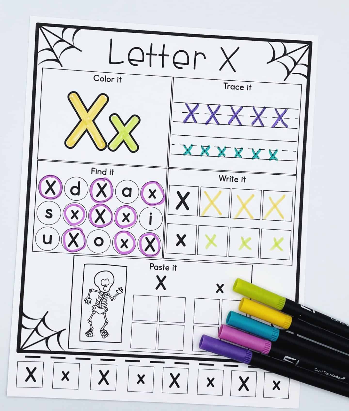 Letter x alphabet worksheet halloween themed, with spider webs in the corners, a place to color, trace, find, write, and paste and a black and white skeleton with 5 different colored pens. 
