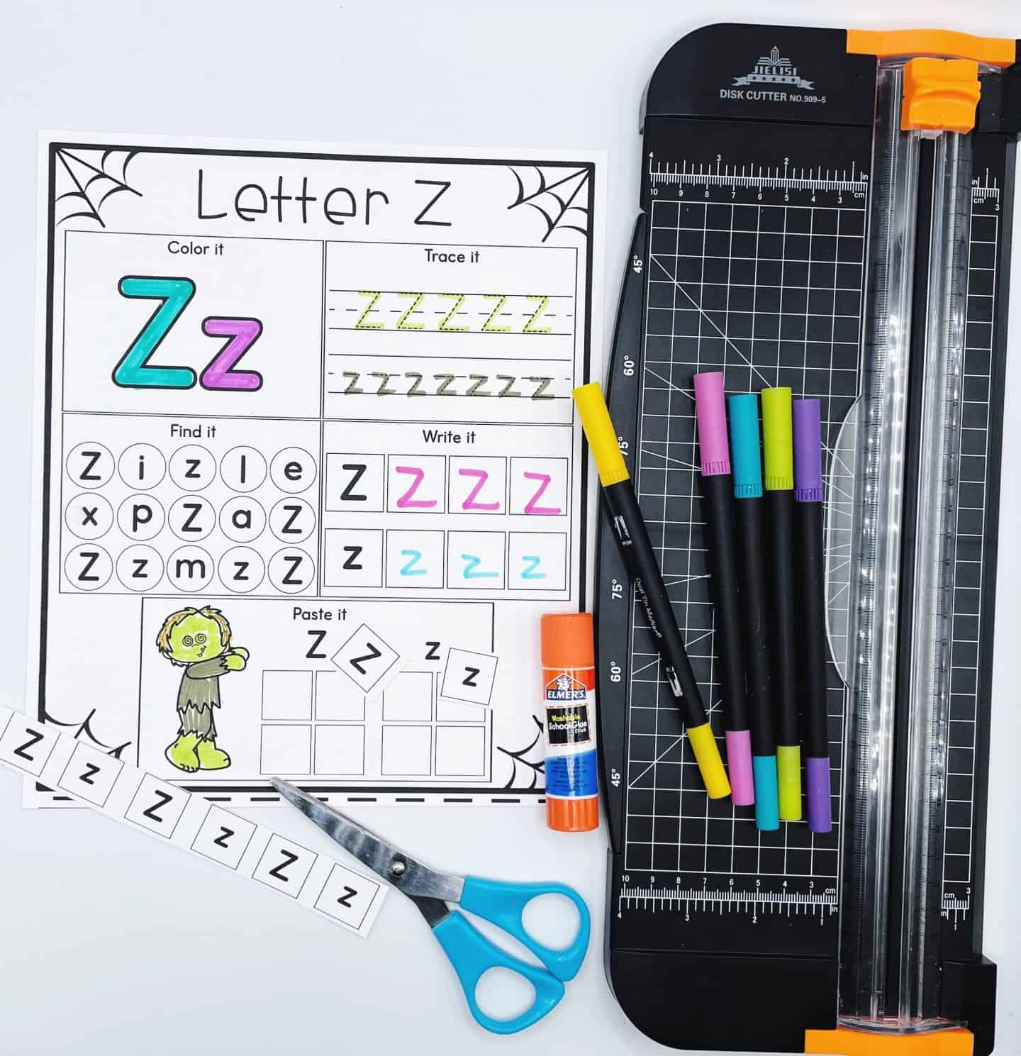 Letter z spooky alphabet worksheets next to a paper cutter, with colored pens on top, some glue, and scissors with the letter z cut out.