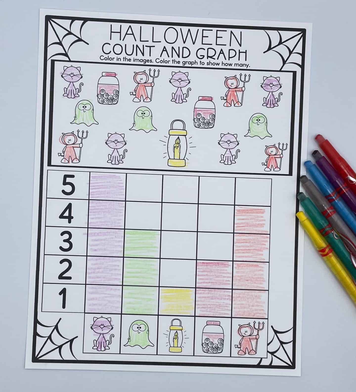 A Halloween-themed “Count and Graph” worksheet featuring cute illustrations of black cats, ghosts, lanterns, candy jars, and devil-costumed characters. Each type of image is counted and graphed using colored pencils, with bars filled in pink, green, yellow, red, and purple. A set of colored pens lies beside the worksheet for a festive and educational touch.