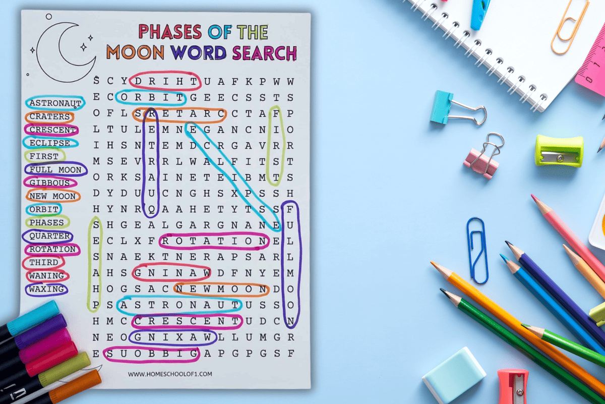 Printable “Phases of the Moon Word Search” activity placed on a light blue desk, surrounded by school supplies like pencils, paper clips, erasers, and markers. The worksheet features a list of moon-related words such as astronaut, crescent, orbit, gibbous, and new moon, with each word highlighted in various colors within the grid. A crescent moon icon decorates the top left corner.