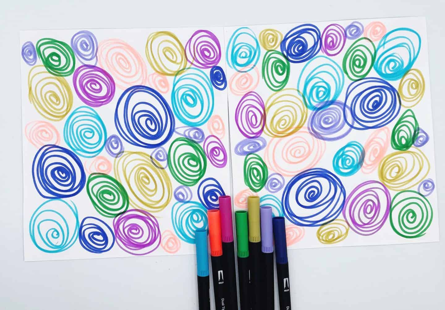 Two printable background sheets covered in colorful hand-drawn spiral doodles in shades of blue, green, purple, yellow, and pink. Below the pages are seven matching marker pens, suggesting this DIY design was made for a craft or printable game like memory cards.