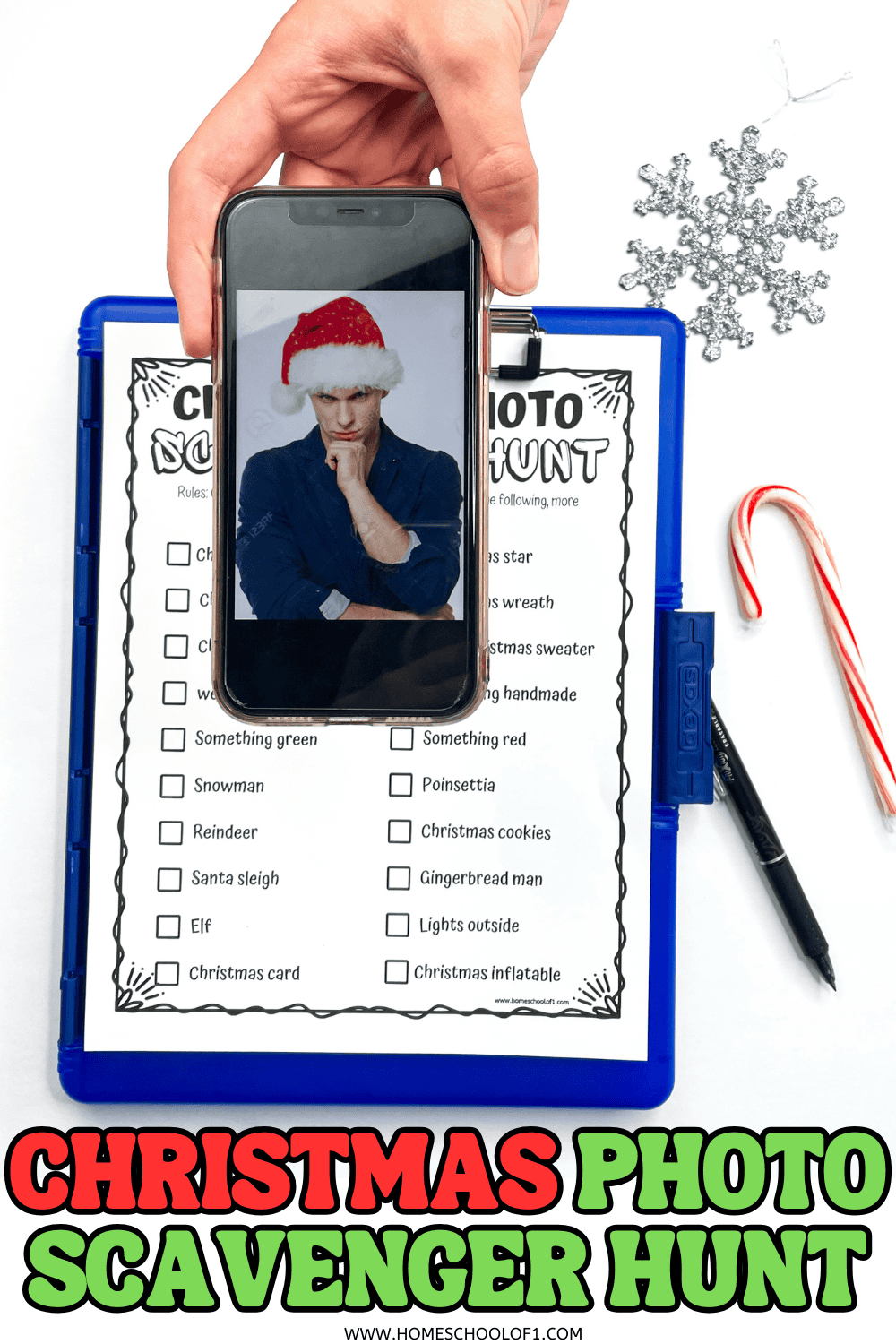 Teen holding phone with Santa selfie over printable Christmas photo scavenger hunt checklist, clipboard, candy cane, and snowflake.

