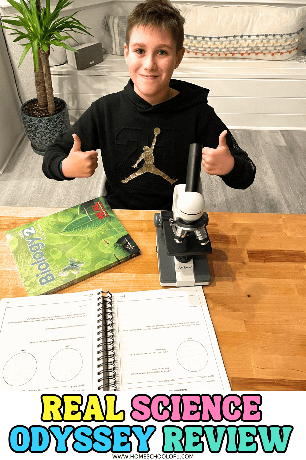 A middle-school student sitting at a table with the Real Science Odyssey Biology 2 textbook, a microscope, and open workbook pages, giving two thumbs up during a homeschool biology lesson.