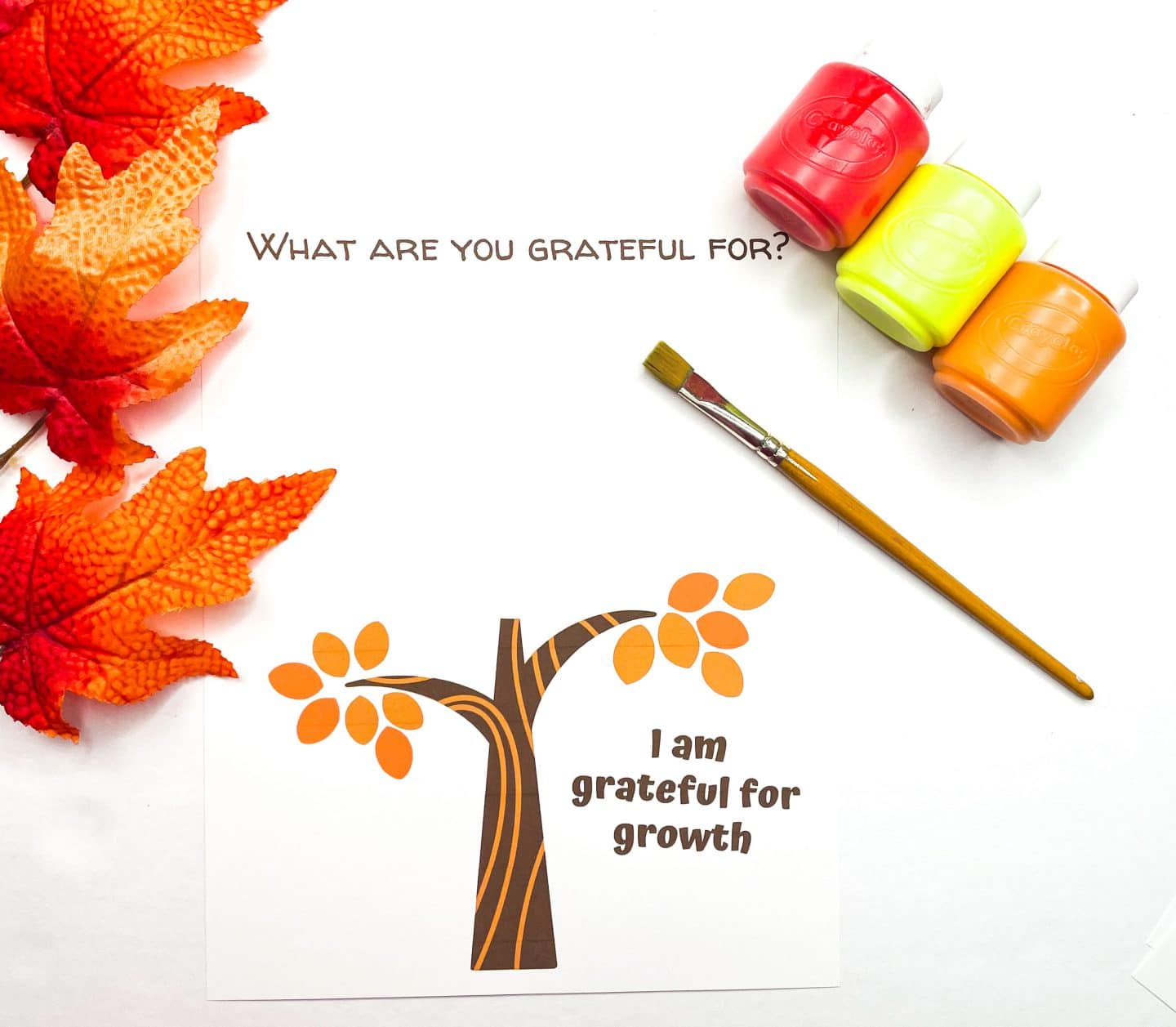 what are you grateful for? then a blank tree with the words I am gratful for growth. A pot of orange red and yellow paint and a paintbrush sit next to the template.