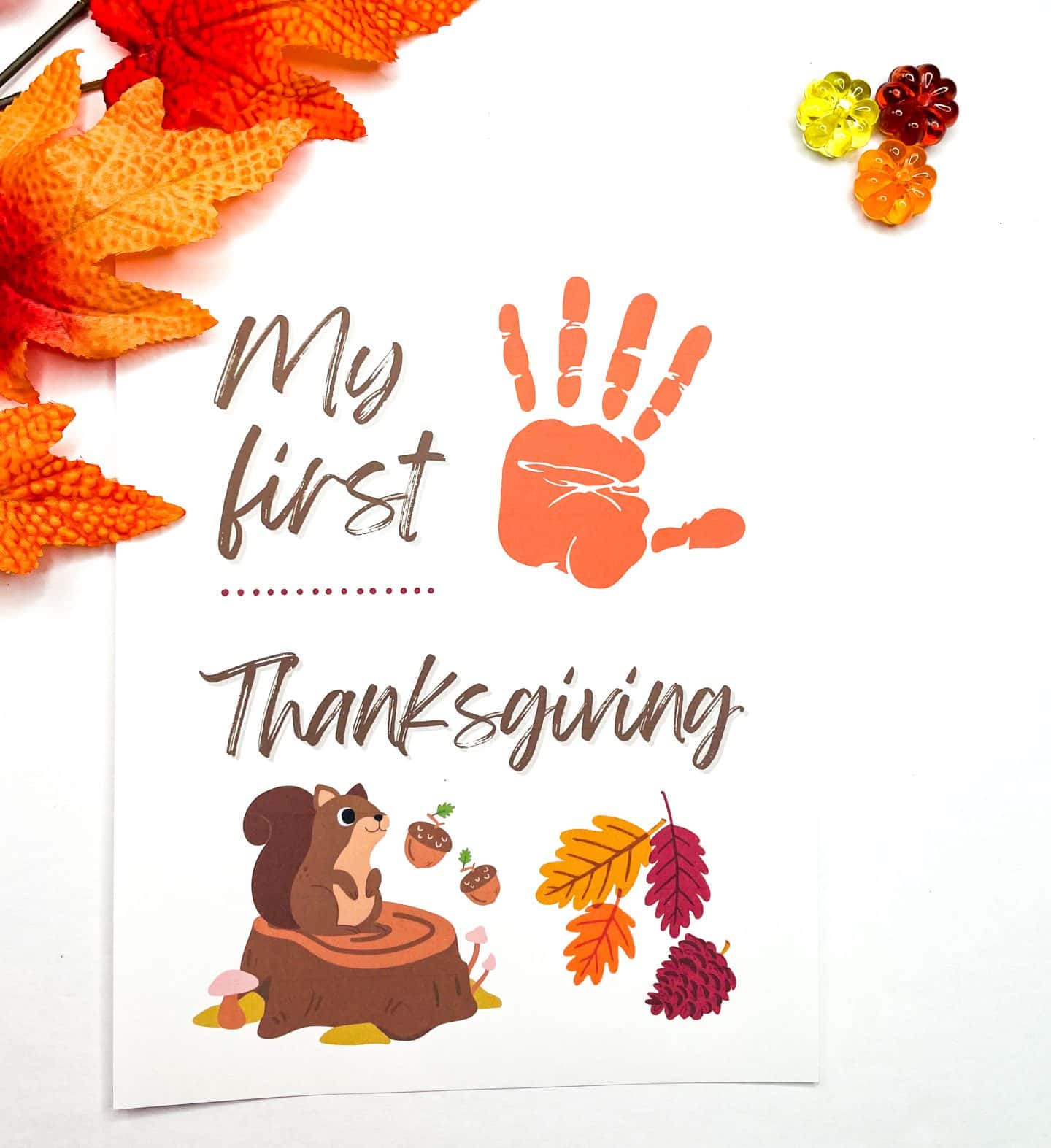 my first thanksgiving handprint art with an orange high 5 handprint. there is a cartoon picture of a squirrel sitting on a tree stump with acorns at the bottom left of the page. 