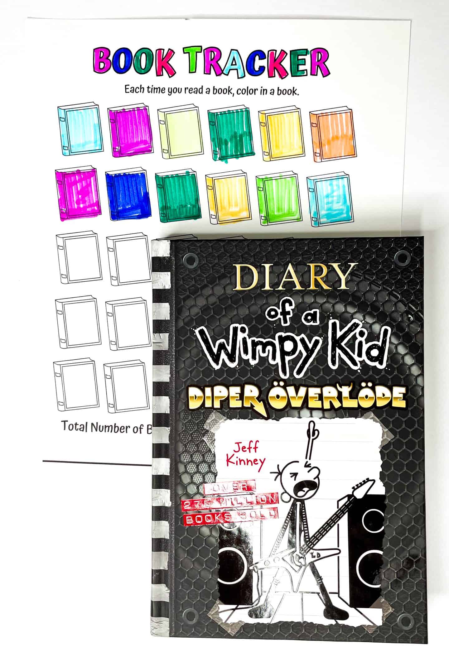 A colorful "Book Tracker" worksheet with rows of book icons to color in as each book is read. Several books are already filled in with bright shades like teal, pink, green, yellow, and blue. Overlapping the worksheet is the book Diary of a Wimpy Kid: Diper Överlöde by Jeff Kinney, featuring a cartoon character playing an electric guitar on a black, hex-patterned background.