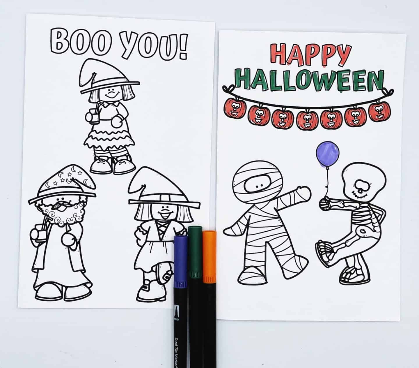 Two Halloween coloring cards with cartoon characters in costumes. The left card reads “Boo You!” and features three uncolored kids dressed as a witch and a wizard. The right card says “Happy Halloween” in red and green, with a jack-o'-lantern garland and two partially colored characters—a mummy and a skeleton holding a purple balloon. Markers in purple, green, and orange are placed below the cards.