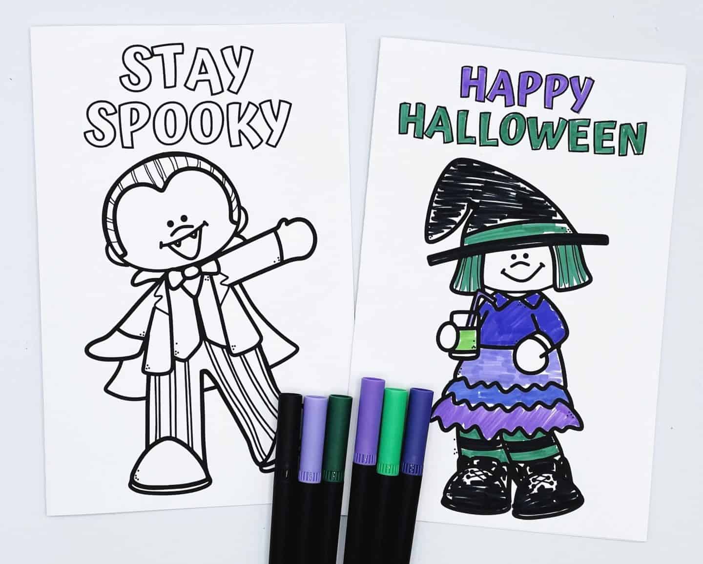 Two Halloween coloring cards with cartoon characters and festive greetings. The left card says “Stay Spooky” and features a cheerful vampire in a striped suit, uncolored. The right card says “Happy Halloween” and shows a smiling witch holding a green drink, dressed in a purple and black outfit with green accents. Purple, green, and black markers are placed below the cards.