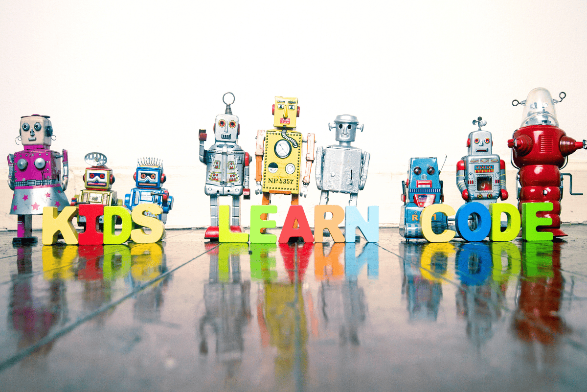 Colorful toy robots lined up on a wooden floor with the words ‘Kids Learn Code’ spelled out in bright letters