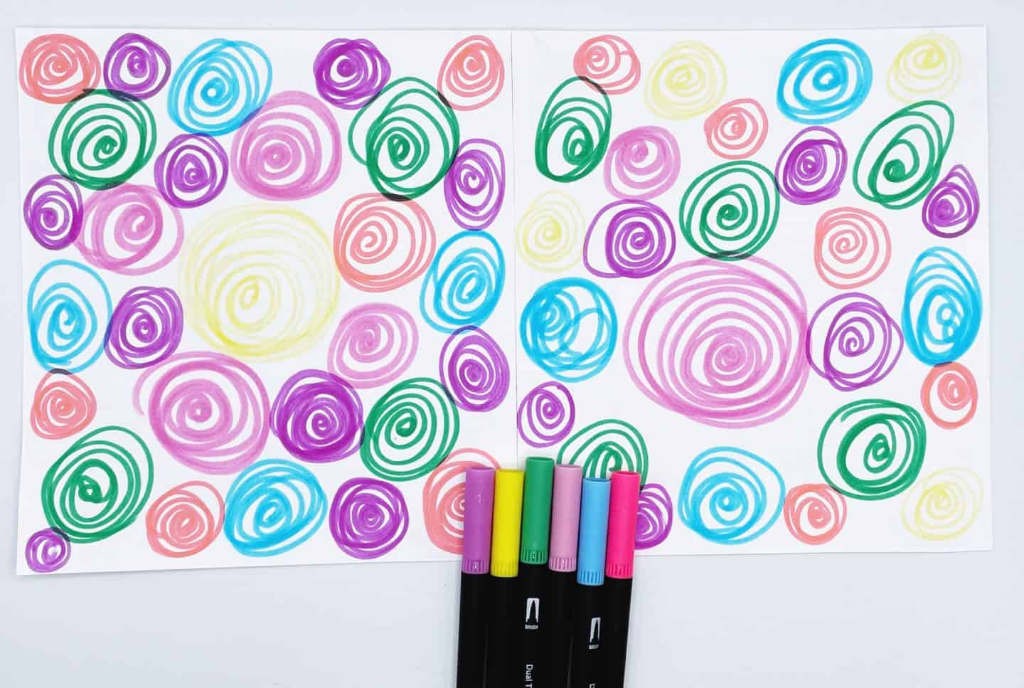 Two sheets of paper filled with colorful spiral doodles in pink, green, blue, purple, yellow, and red, lying side by side. A set of six dual-tip markers in matching colors is placed at the bottom center of the image, suggesting they were used for the artwork.