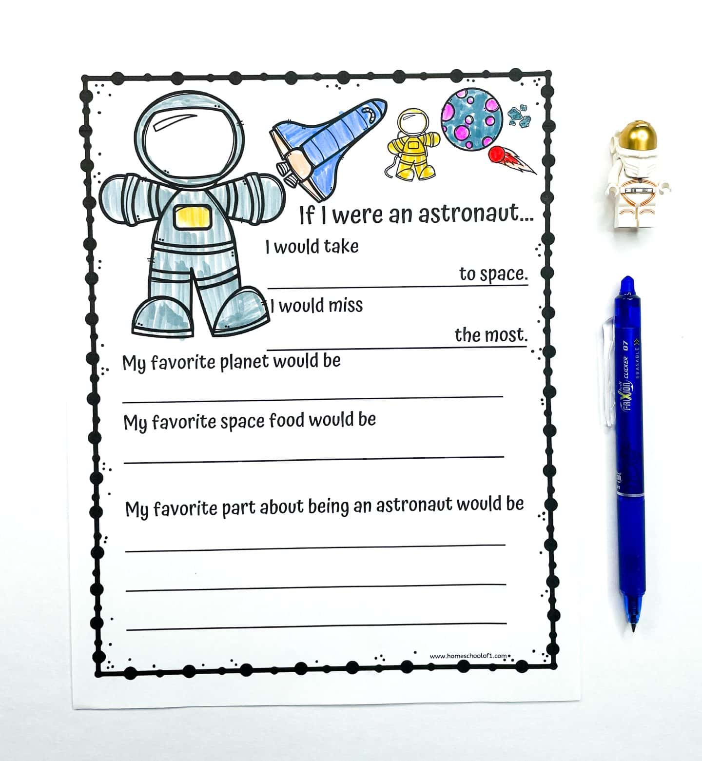 A fun "If I Were an Astronaut" printable worksheet for kids featuring prompts like what they would take to space, what they'd miss most, favorite planet, favorite space food, and favorite part about being an astronaut. The page is decorated with cartoon-style drawings of an astronaut, space shuttle, rocket, and planets, and is accompanied by a blue pen and a small astronaut toy figure.

