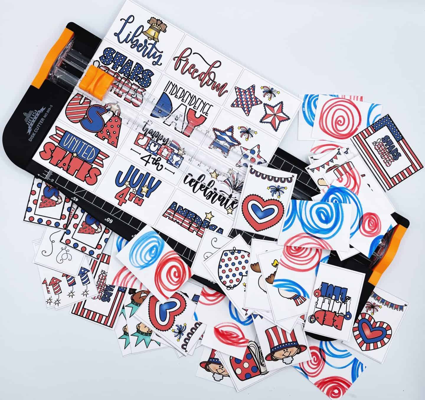 A printable Fourth of July memory game being cut with a paper trimmer, featuring colorful cards with red and blue swirl backs and festive front designs including “Liberty,” “Freedom,” “July 4th,” fireworks, patriotic hats, hearts, the word “USA,” and cartoon characters in Independence Day outfits.