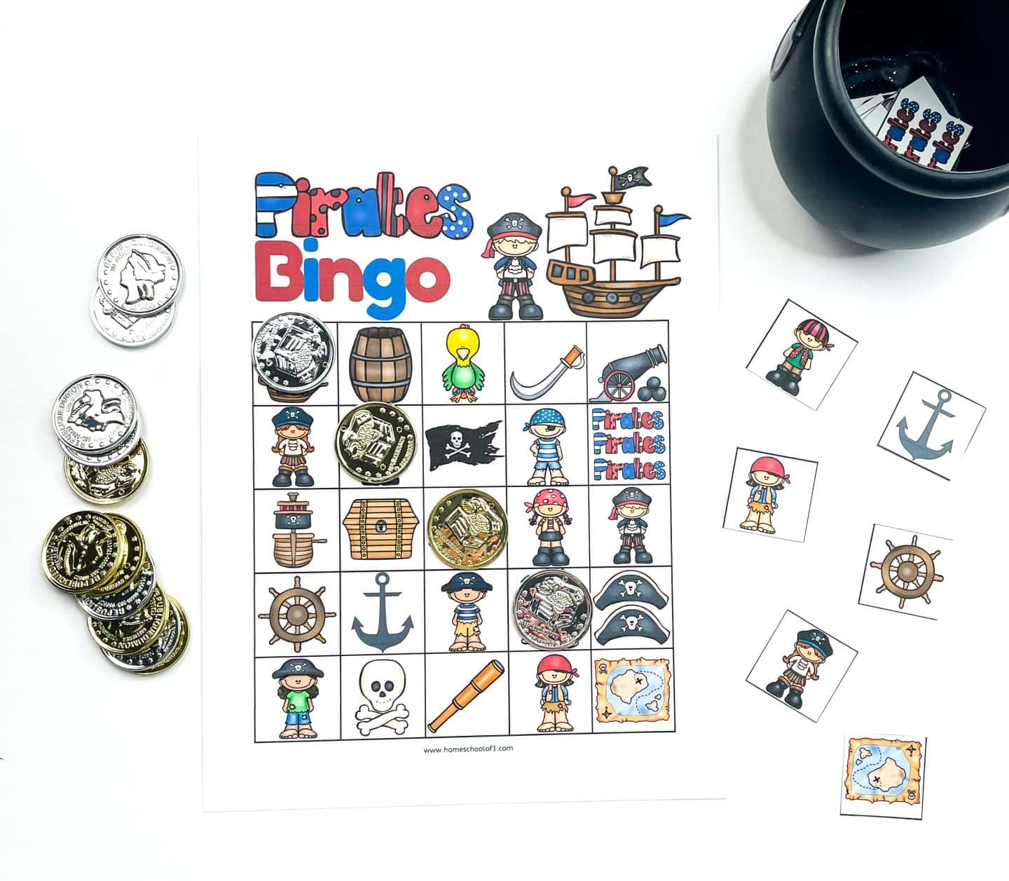Pirate-themed bingo game in progress, featuring a colorful card filled with illustrations like a treasure chest, pirate, anchor, skull, map, and cannon. Silver and gold plastic coins are used as bingo markers, and a small black pot holds the square calling cards, some of which are laid out nearby.